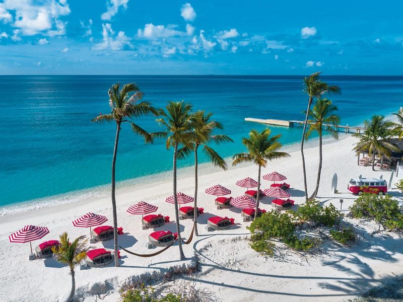 Sandstrand mit Palmen und pinken Sonnenschirmen am blauen Meer.