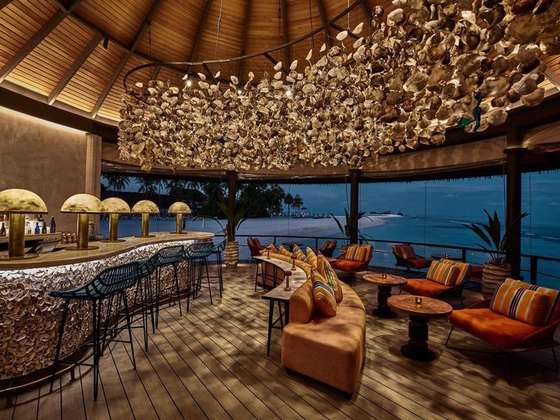 Offene Strandbar mit gemütlichen Sitzgelegenheiten und Blick auf das Meer bei Nacht.