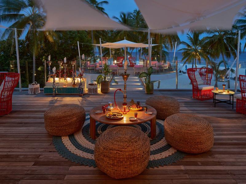 Gemütlicher Outdoor-Loungebereich mit runden Sitzkissen und Kerzenlicht auf Holzterrasse bei Dämmerung.
