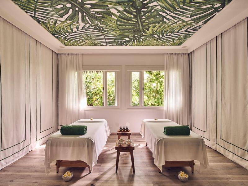 Ein ruhiger Spa-Raum mit zwei Massageliegen und tropischem Blätterdekor an der Decke.