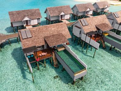 Bungalows auf Stelzen mit braunen Dächern über klarem, türkisfarbenem Wasser, verbunden durch Stege.