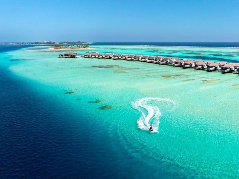 Domki na wodzie w przejrzystej, niebieskiej wodzie z motorówką zostawiającą biały ślad.