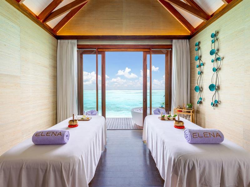 Pokój spa z dwoma stołami do masażu naprzeciw dużego okna z widokiem na ocean.