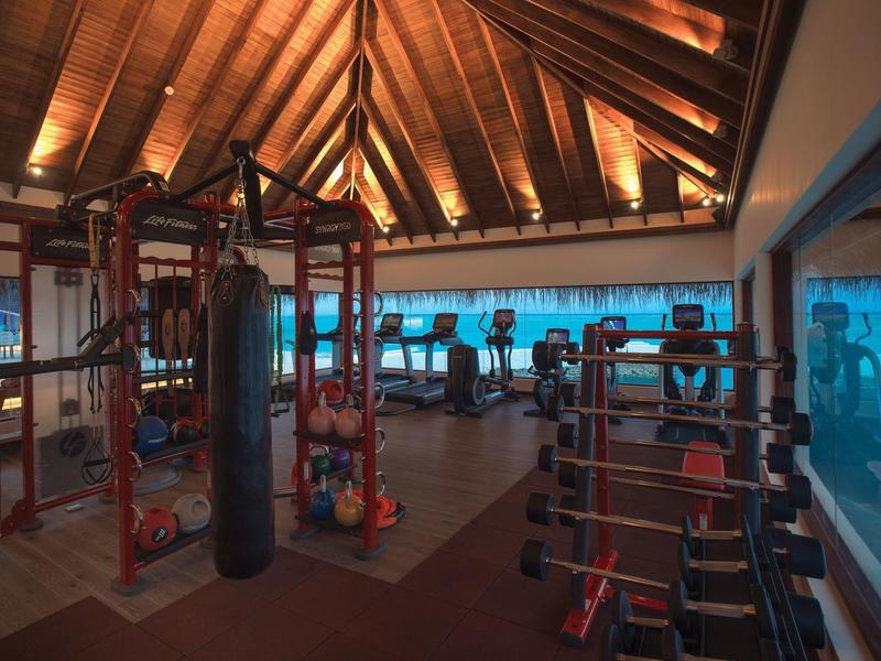 Przestronna siłownia z drewnianym sufitem, sprzętem cardio, ciężarami i workiem treningowym w hotelu.