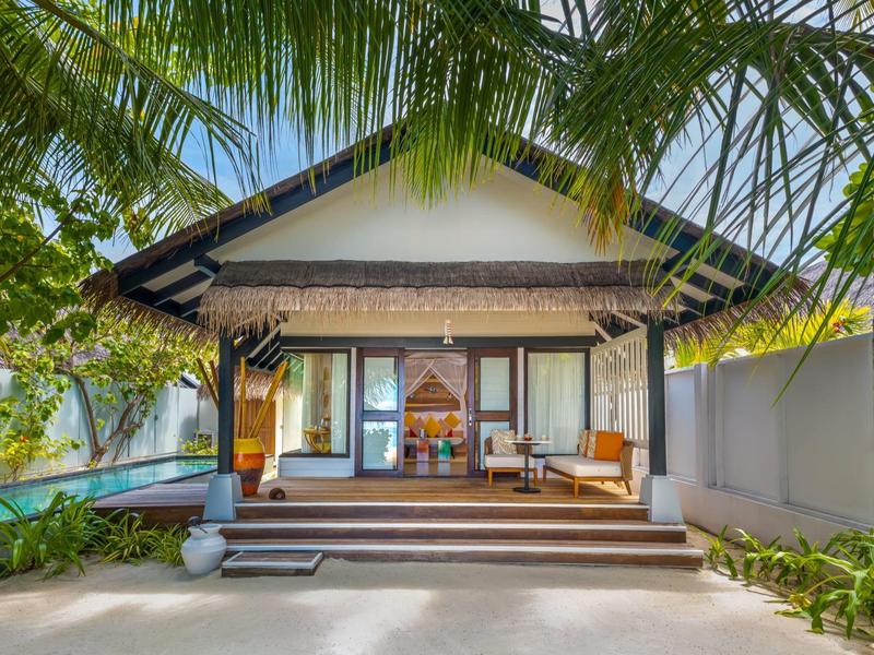 Luksusowy bungalow z drewnianym tarasem, wygodną częścią wypoczynkową i tropikalnymi palmami.