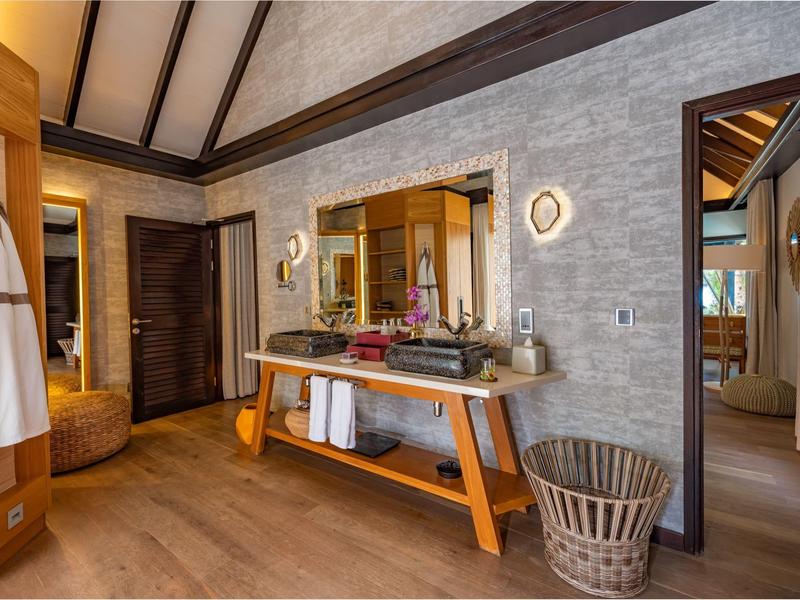 Przytulna łazienka z drewnianą podłogą, dużym lustrem, kamienną ścianą i wiszącymi ręcznikami.