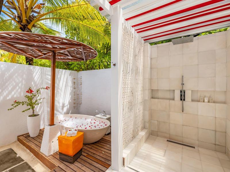 Zewnętrzny prysznic z kafelkowanymi ścianami, drewnianym parasolem i wygodnym siedzeniem pod palmami.
