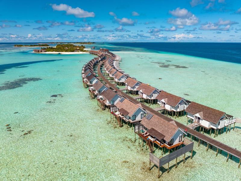 Bungalowy nad wodą na czystym turkusowym morzu pod niebieskim niebem z rozproszonymi chmurami.