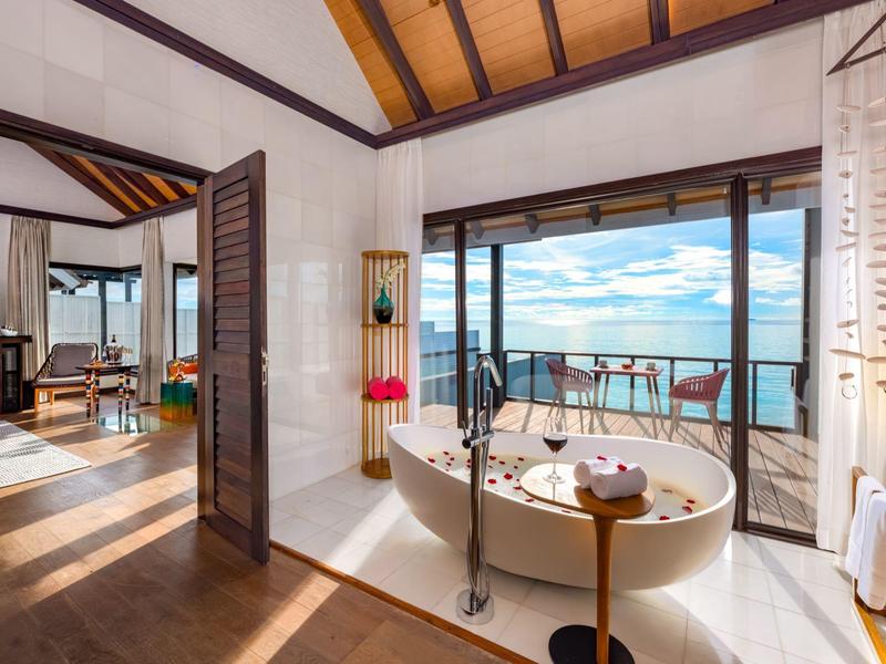Luksusowa łazienka z dużą wanną i widokiem na ocean przez otwarte szklane drzwi.
