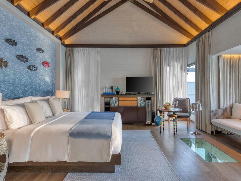 Przestronny pokój hotelowy z dużym łóżkiem, telewizorem, sofą, drewnianym sufitem i widokiem na ocean.