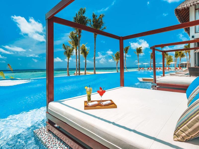 Leżanki przy basenie z napojami z widokiem na ocean i palmy w słoneczny dzień.