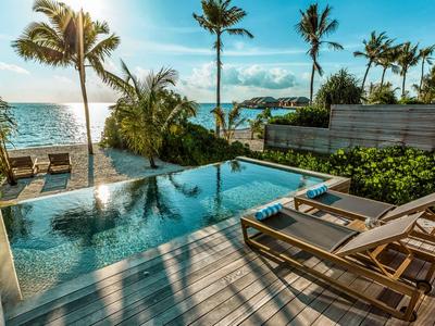 Área de piscina de lujo con sillas reclinables y vistas al mar al atardecer.