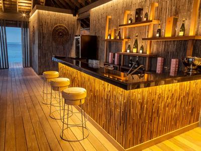 Bar moderna con bancone in legno e sgabelli gialli in un resort tropicale al crepuscolo.