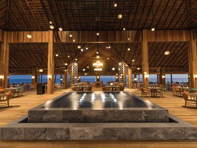 Gran área de comedor abierta con techo de madera y mesas elegantes junto al agua.