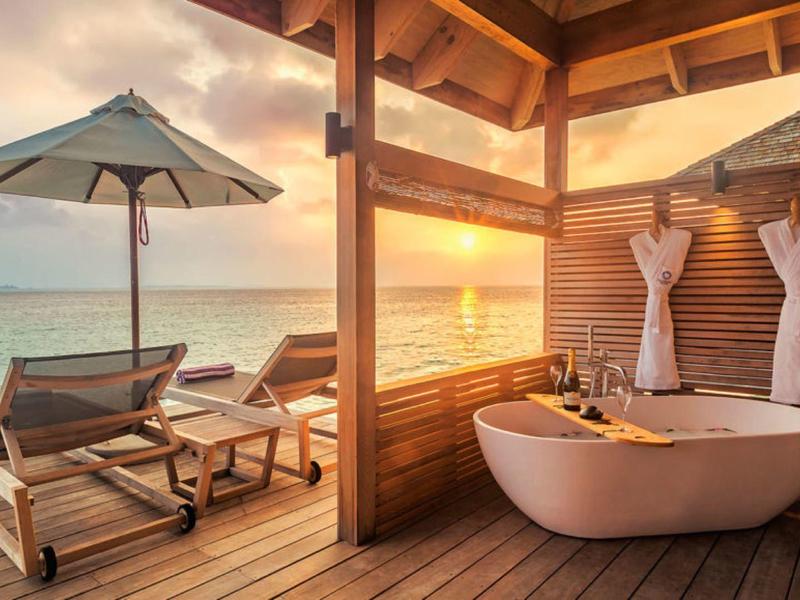 Terrazza in legno con vasca indipendente e lettini prendisole con vista sul mare al tramonto