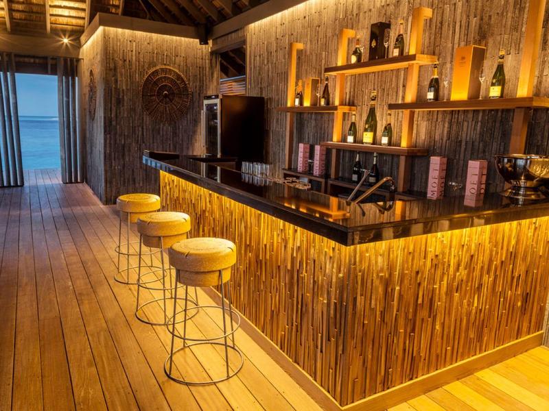 Bar moderna con bancone in legno e sgabelli gialli in un resort tropicale al crepuscolo.