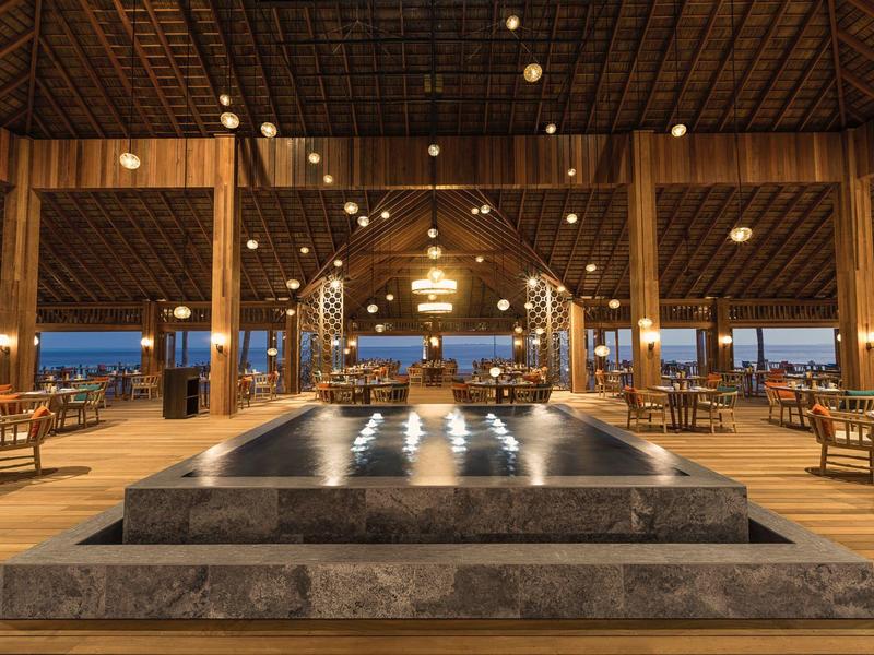 Area lobby aperta dell'hotel con tetto in legno, fontana illuminata e aree salotto eleganti.