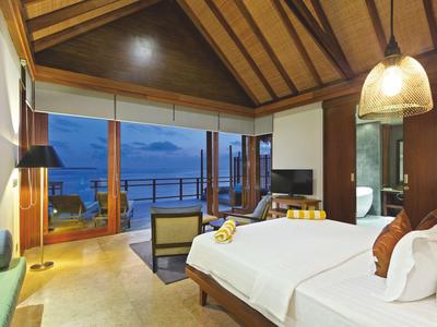 Habitación de hotel de lujo con cama grande y terraza con vistas al mar al atardecer.