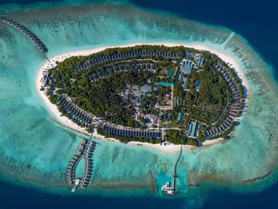 Vista aérea de una isla tropical con playa, edificios de resort y muelles en agua turquesa.