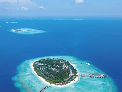 Vista aérea de una pequeña isla tropical con mar azul claro y un muelle largo.