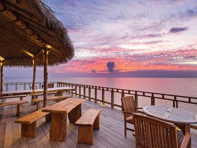 Drewniany taras z miejscami do siedzenia z widokiem na ocean o zachodzie słońca.