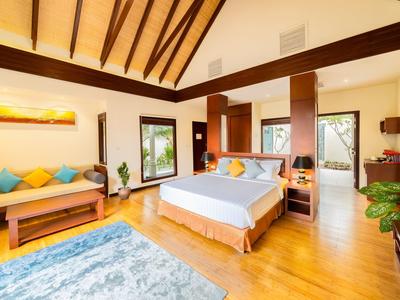 Habitación de hotel luminosa con suelo de madera, cama doble, sofá, alfombra y grandes ventanas con vista al verde.