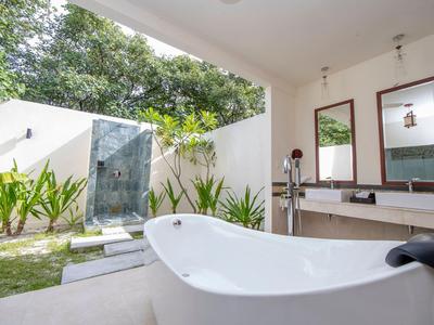 Bañera independiente en un baño moderno con vista abierta a un jardín y una ducha exterior.