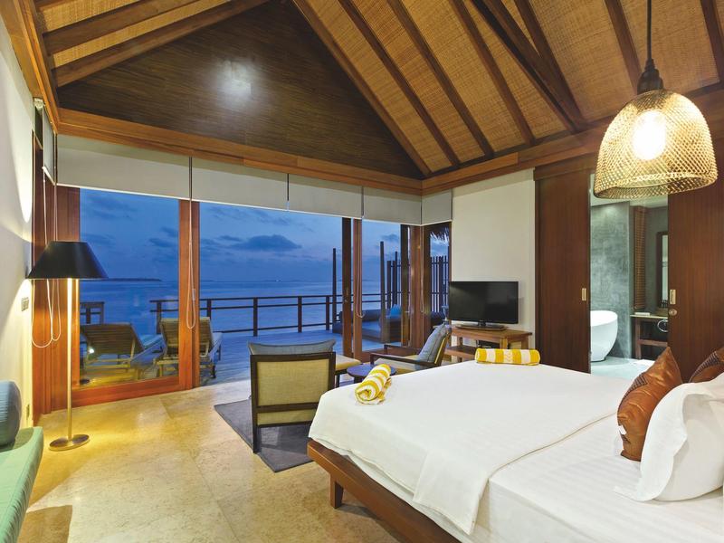 Habitación de hotel de lujo con cama grande y terraza con vistas al mar al atardecer.