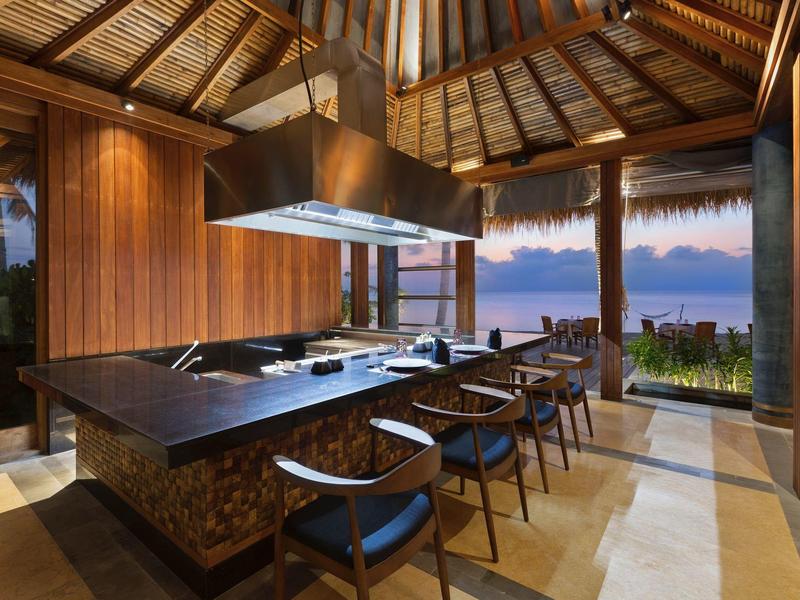 Cocina abierta con techo de madera y vista al mar al atardecer en un hotel.