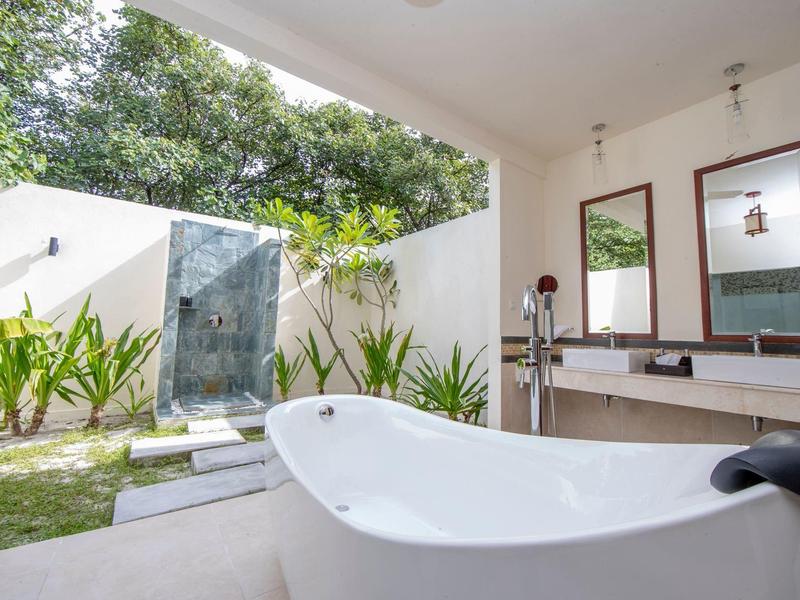 Bañera independiente en un baño moderno con vista abierta a un jardín y una ducha exterior.