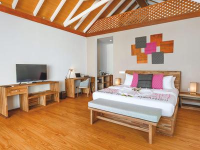 Helles, modernes Hotelzimmer mit Holzmöbeln, Doppelbett, Fernseher und Schreibtisch unter sichtbaren Holzbalken.