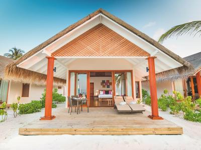 Blick auf einen Bungalow mit Terrasse am Strand und tropischer Vegetation.