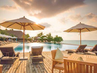 Poolbereich mit Sonnenliegen, Sonnenschirmen und Meerblick bei Sonnenuntergang