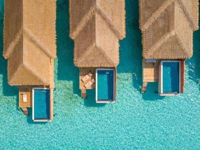 Widok z lotu ptaka na bungalowy z basenami nad przejrzystą, niebieską wodą.