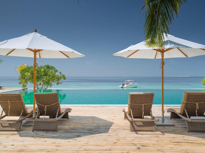 Strefa basenowa z leżakami i parasolami przy spokojnym morzu.