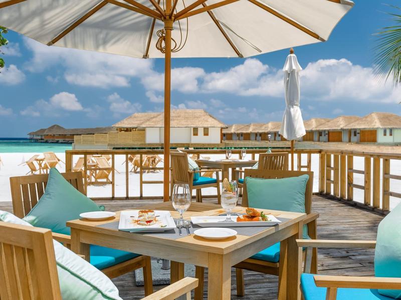 Drewniany taras z stołem i parasolem, widok na hotel nad wodą.