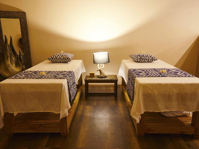 Dwa pojedyncze łóżka z białą pościelą i poduszkami obok małego stolika z lampą.