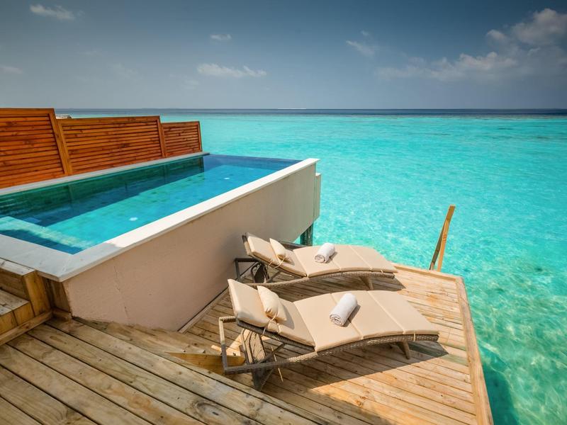 Drewniany taras z basenem i leżakami nad przejrzystym, turkusowym morzem pod niebieskim niebem.