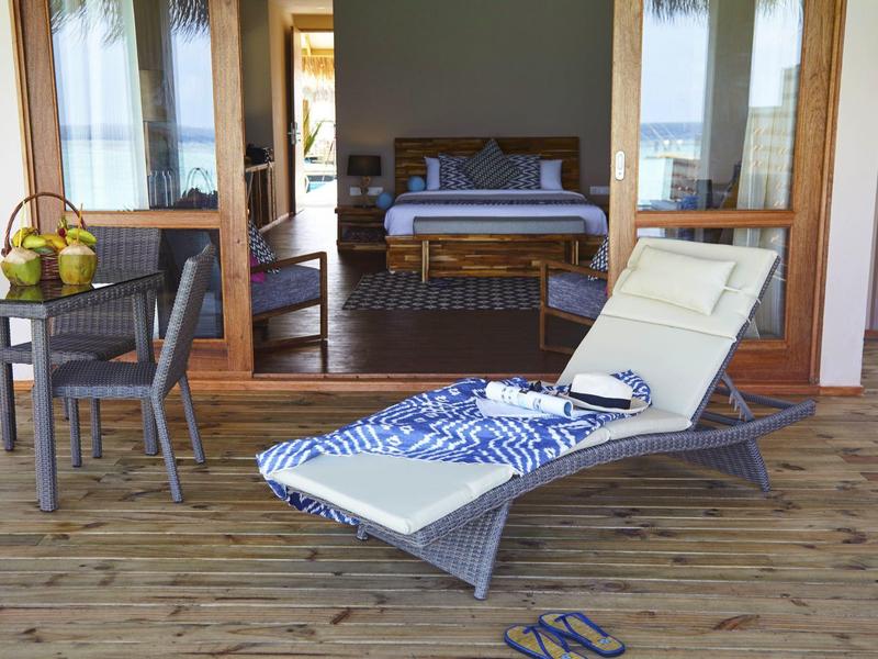 Nowoczesne krzesło i stół na drewnianym tarasie przed otwartym pokojem z łóżkiem