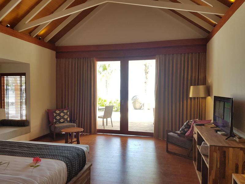 Jasny pokój hotelowy z odsłoniętymi belkami, łóżkiem podwójnym, częścią wypoczynkową i widokiem na taras.