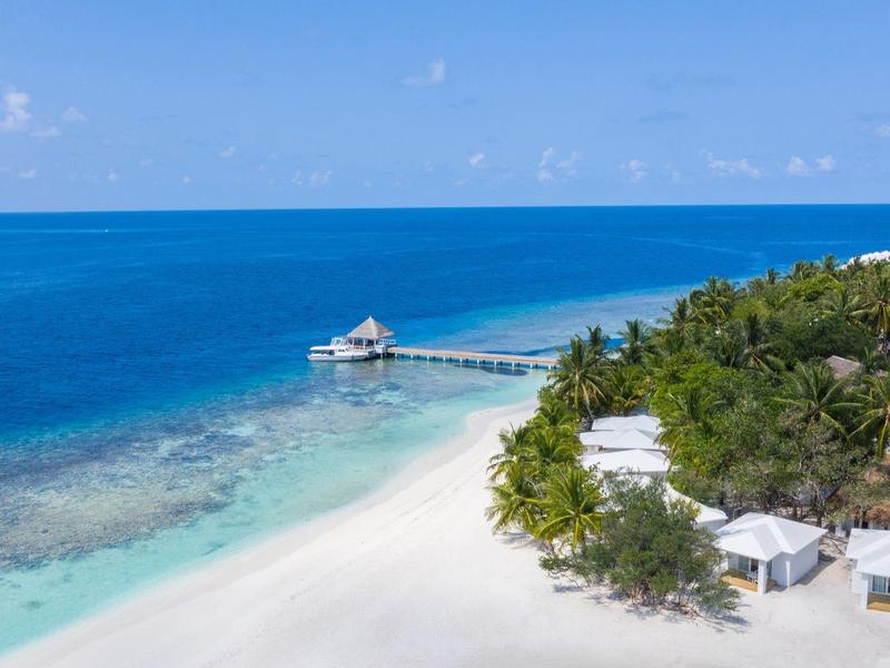 Weißer Sandstrand mit klarem blauen Wasser und einem Pier mit Hütte im tropischen Urlaubsort.