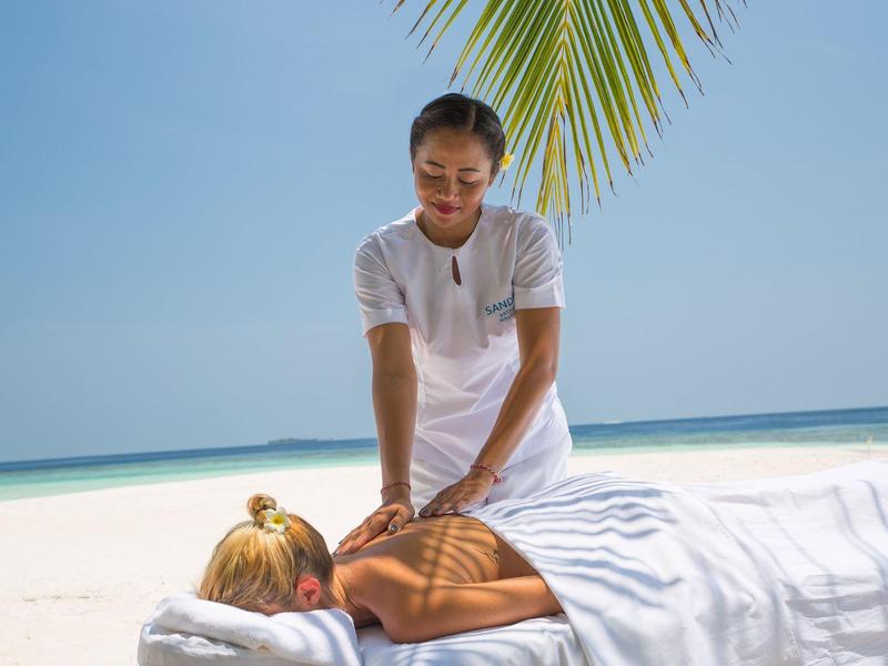 Frau erhält Massage am Strand unter Palmen mit Blick auf das Meer.