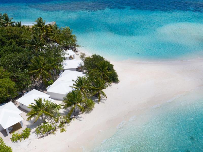 Weiß gedeckte Bungalows am tropischen Strand mit klarem, türkisfarbenem Wasser.