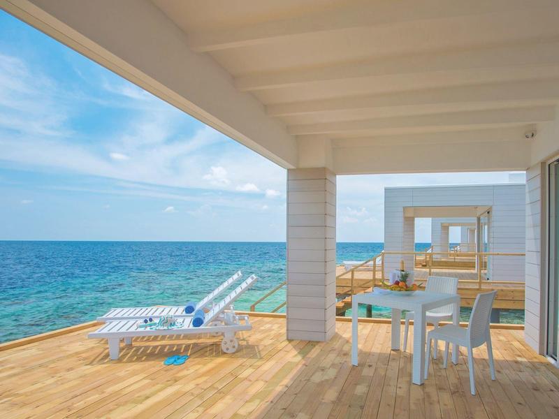 Terrasse mit Esstisch und Liegestühlen mit Blick auf das Meer unter blauem Himmel.