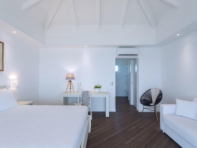 Helles Hotelzimmer mit Doppelbett, weißer Couch, Stuhl und Zimmerbeleuchtung.