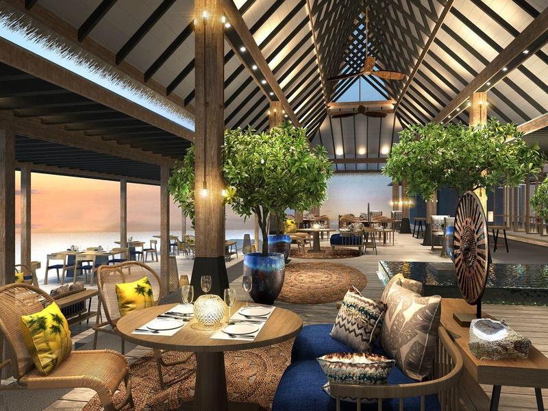 Espace lounge ouvert avec poutres en bois, canapés confortables et vue sur le coucher de soleil en mer.
