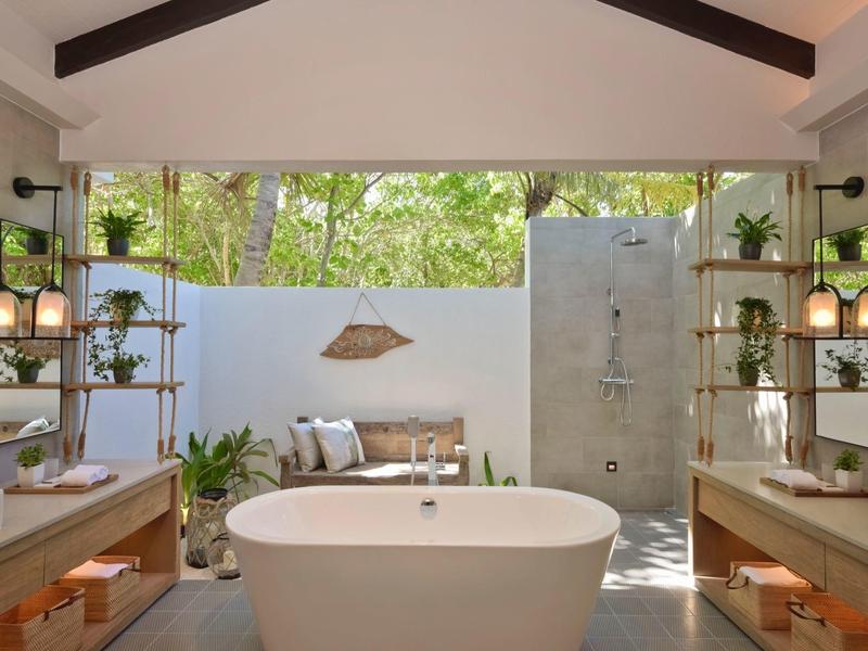 Salle de bain moderne avec baignoire autoportante, étagères ouvertes et douche extérieure dans un cadre tropical.