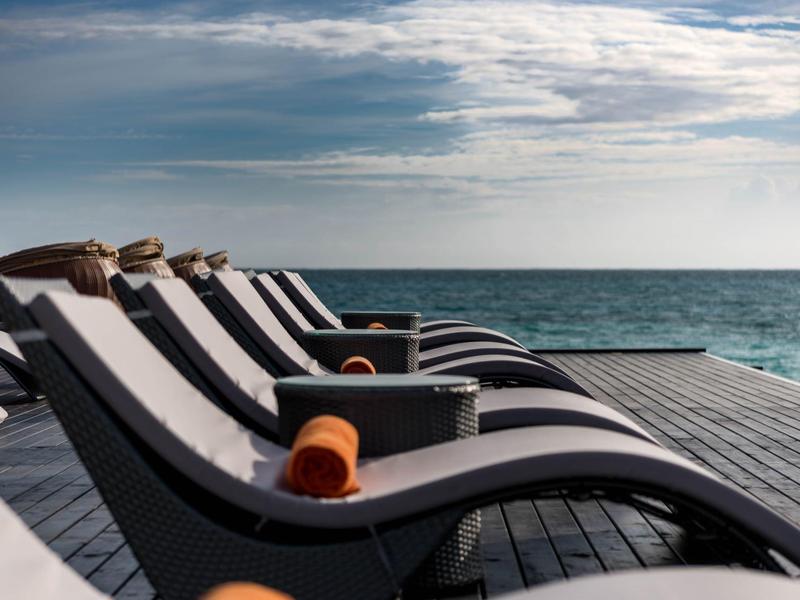 Chaises longues vides avec serviettes sur une terrasse au bord de la mer sous un ciel nuageux.