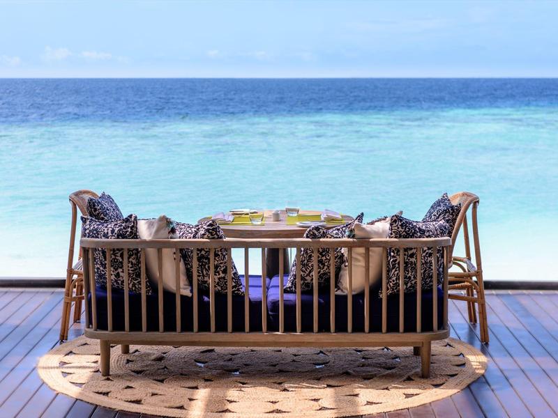 Coin salon confortable sur terrasse en bois avec vue sur la mer turquoise.