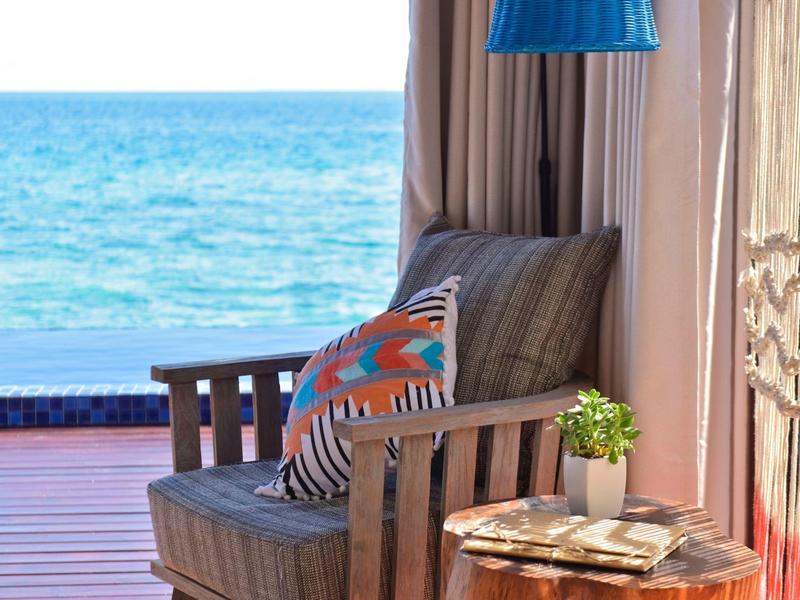 Fauteuil confortable avec coussins à côté d'une petite table avec plante et vue sur la mer.